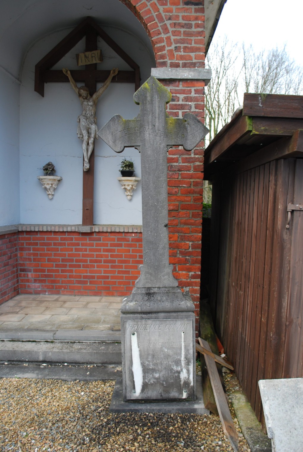 Grafsteen met kruis en een beeld van Jezus aan het kruis in een bakstenen nis.