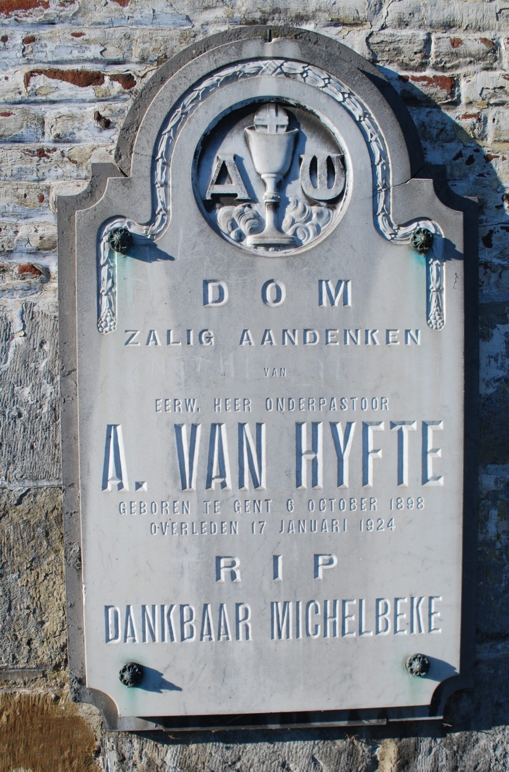 Gedenksteen voor onderpastoor A. Van Hyfte, geboren 1898, overleden 1924, met religieuze symbolen.