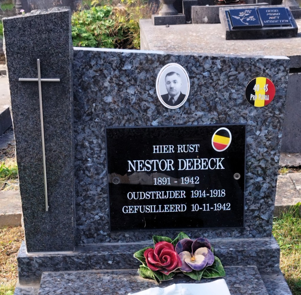 Grafsteen van Nestor Debeck (1891-1942), oudstrijder WOI, gefusilleerd in 1942, met kruis en bloemen.