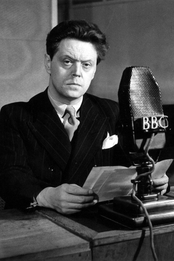 Zwarte-witfoto van een man in pak die een radioboodschap voor de BBC voorbereidt met een microfoon voor zich.