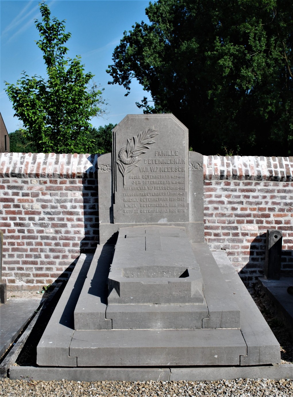 Grafsteen van de familie Detemmerman van Wy Meersch, omgeven door een bakstenen muur en bomen op de achtergrond.