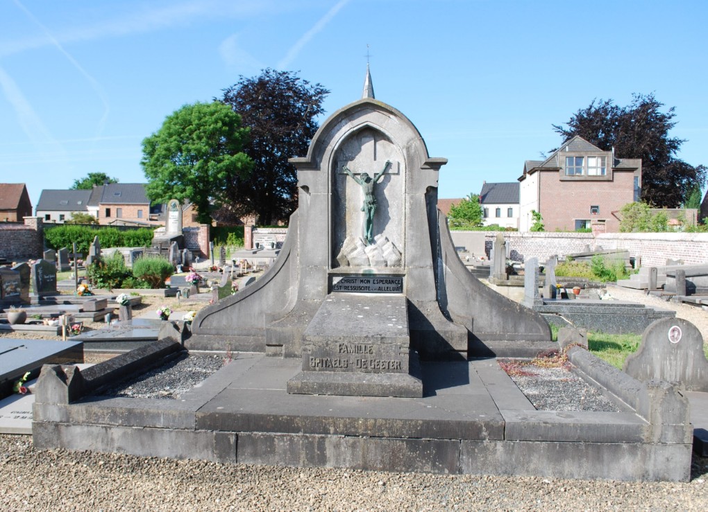 Grafmonument met een kruisbeeld en inscripties op een begraafplaats bij helder weer.