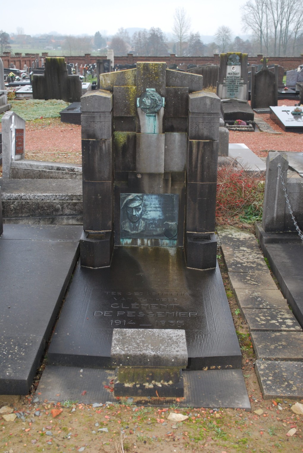 Grafsteen van Clément De Pesseniër (1914-1935) op een begraafplaats met meerdere graven en een mistige achtergrond.
